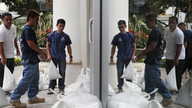 Workers stack sandbags in front of a closed store in preparation for Hurricane Lane, Thursday,...
