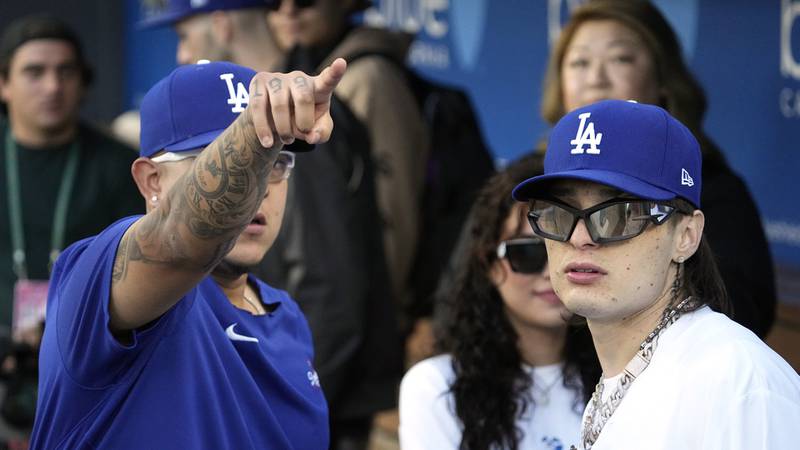 Rapper Peso Pluma, right, talks to starting pitcher Julio Urias in the dugout before throwing...